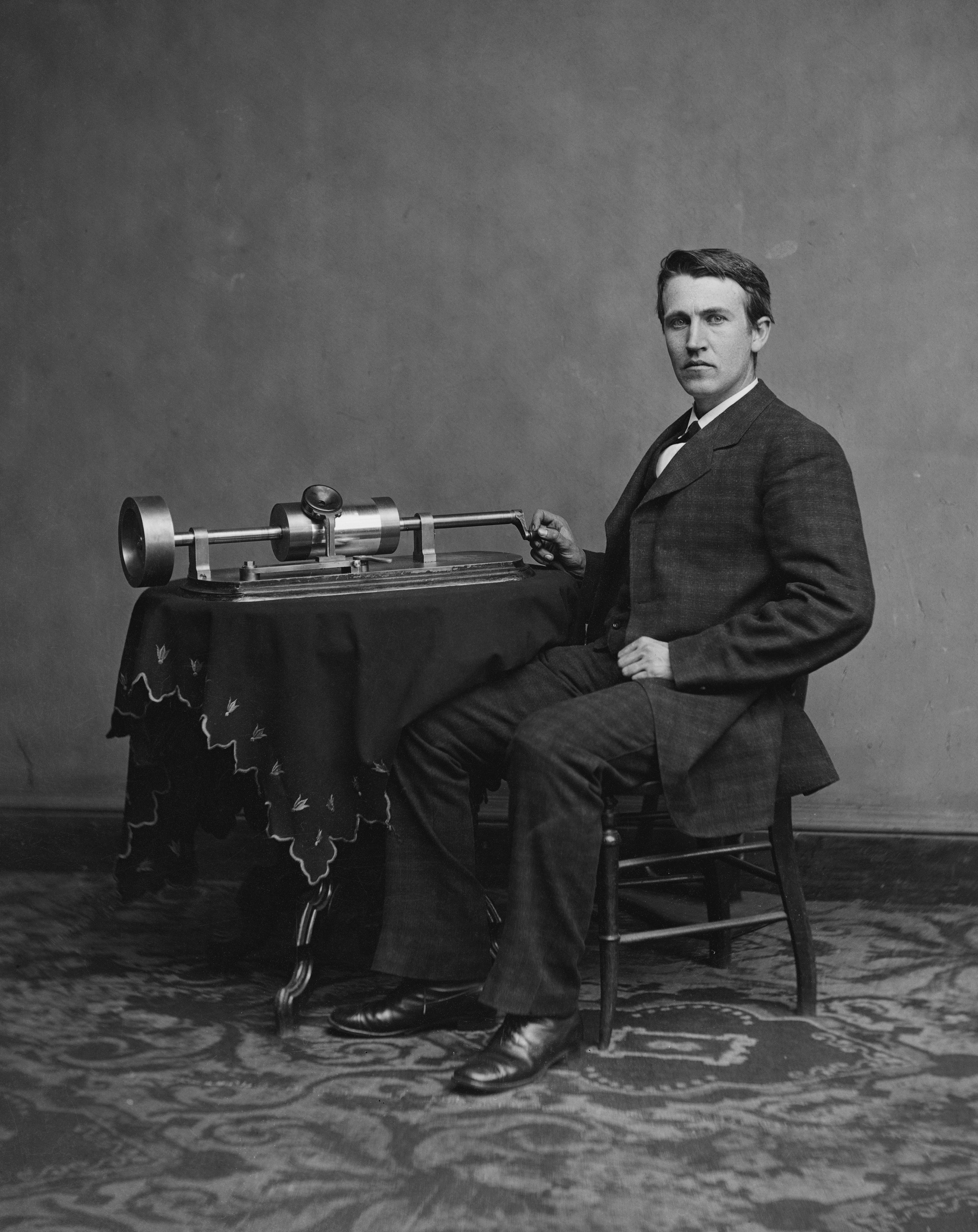 Thomas Edison seated beside an early phonograph.