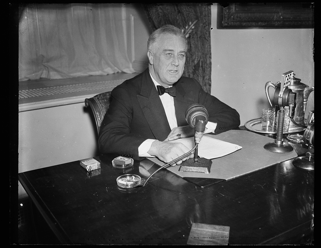 Franklin D. Roosevelt seated at a desk during a radio broadcast.